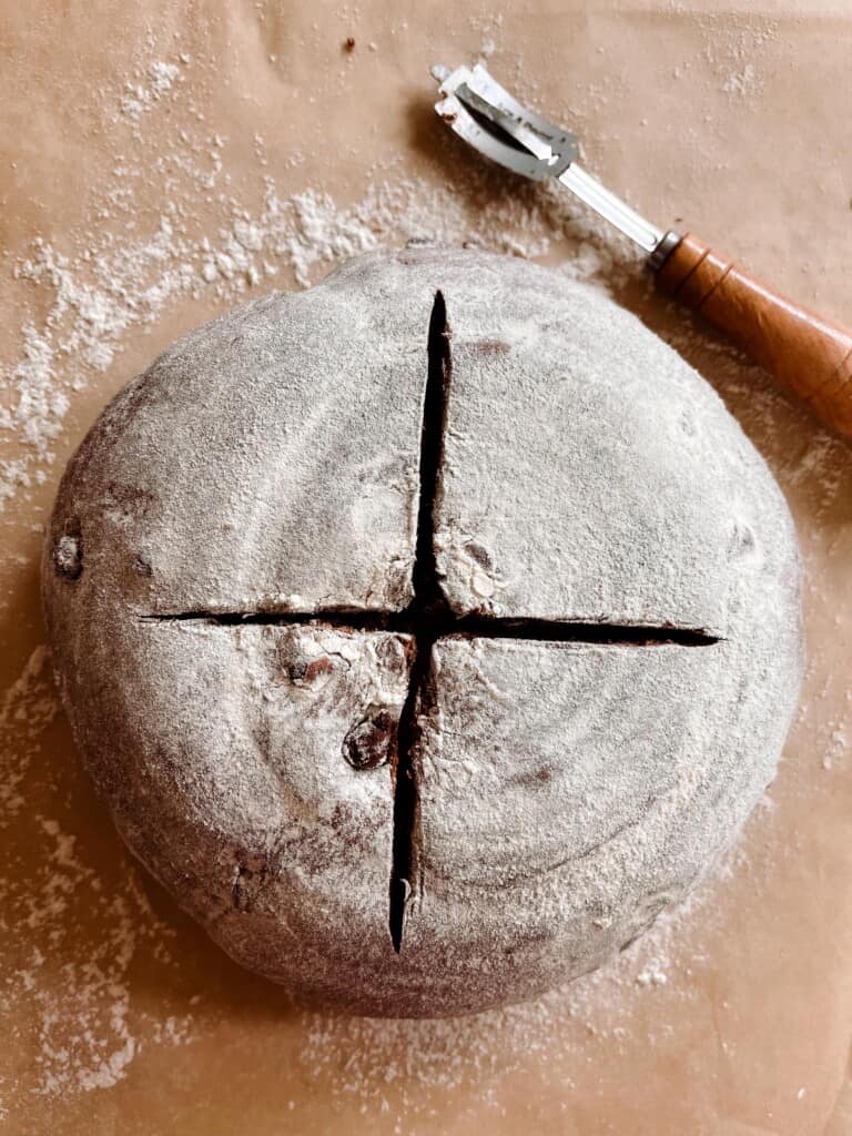 chocolate sourdough bread dusted with flour and scored with a cross on parchment paper
