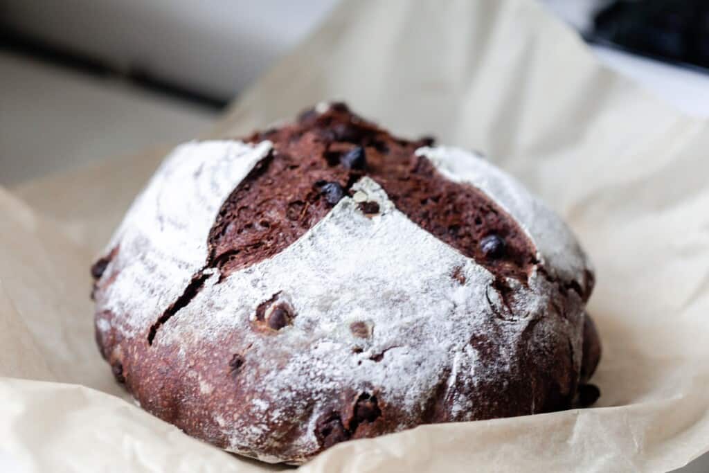 side view of a loaf of sourdough chocolate bread on parchment paper with an antique stove in the background
