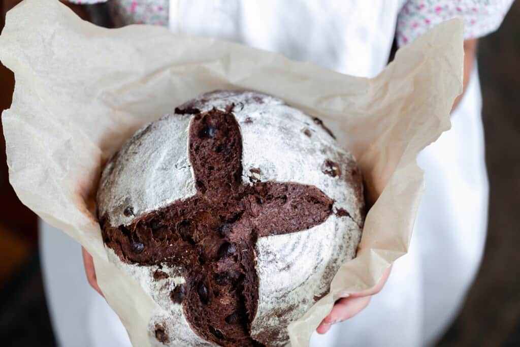 girl holding a parchment lined loaf of chocolate sourdough bread