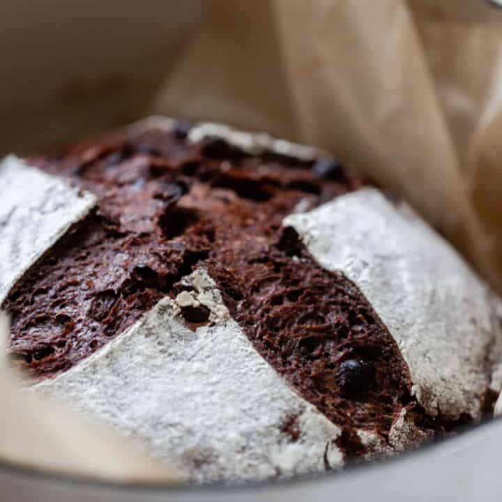 side view of a loaf of chocolate sourdough bread in a parchment lined dutch oven