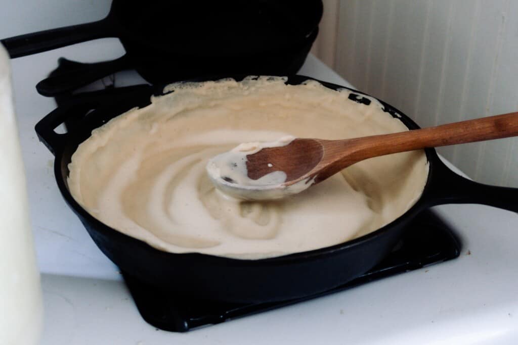 sourdough starter spread in a cast iron skillet with a wooden spoon