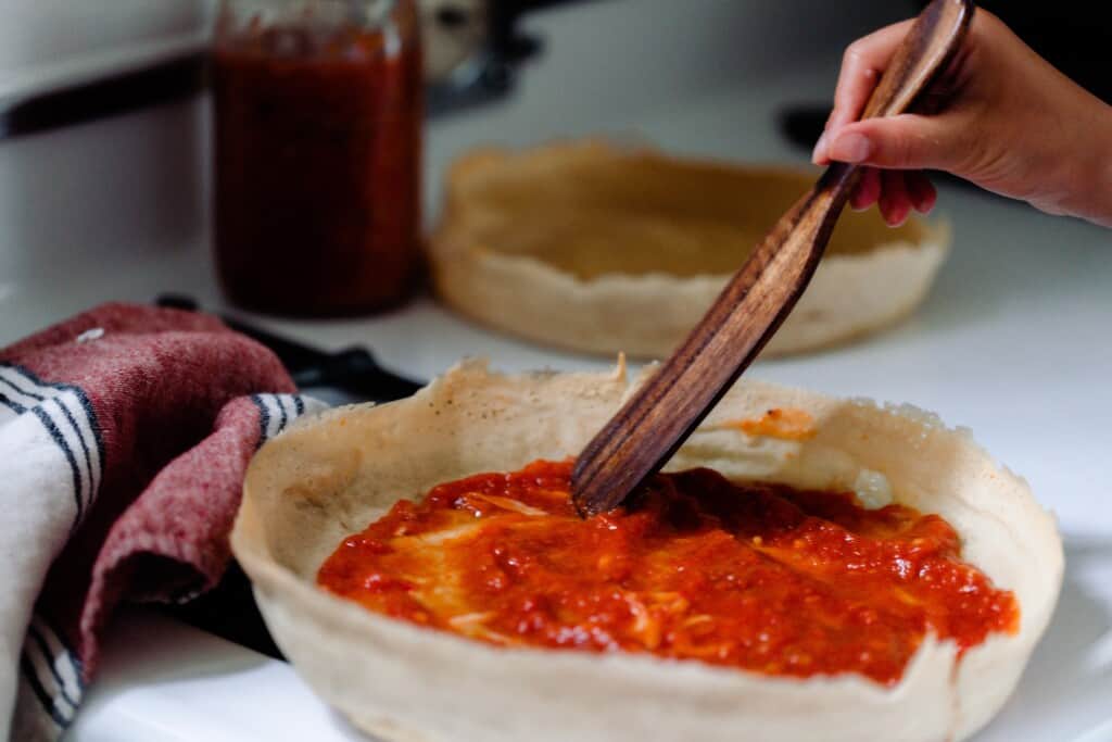a wooden spoon spreading pizza sauce on a sourdough discard pizza crust.