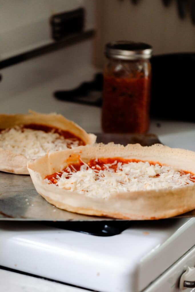 two sourdough pizzas topped with sauce and cheese on a baking sheet on a white oven