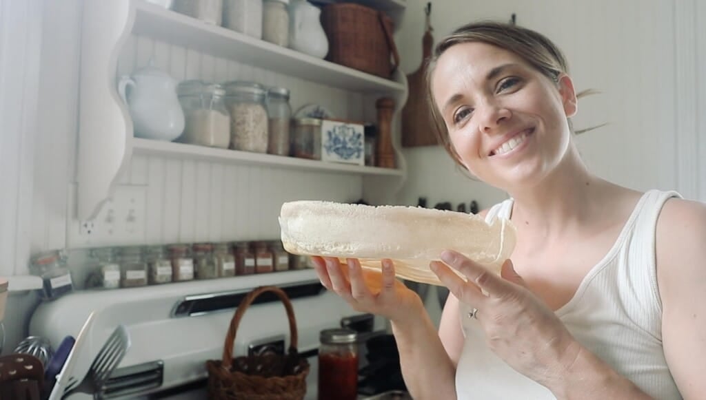 Woman wearing a white tank holding a sourdough pizza crust while smiling