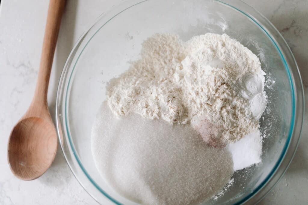 dry ingredients in a glass bowl on a white countertop with a wooden spoon to the left