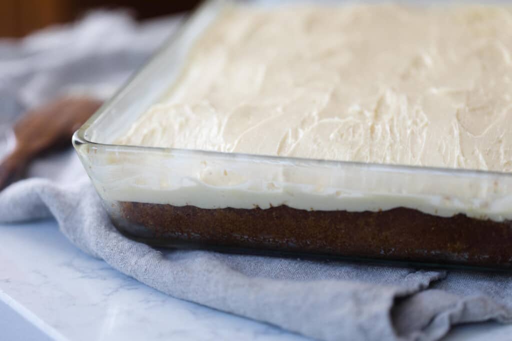 side view of vanilla cake with buttercream frosting in a glass baking dish on a gray napkin