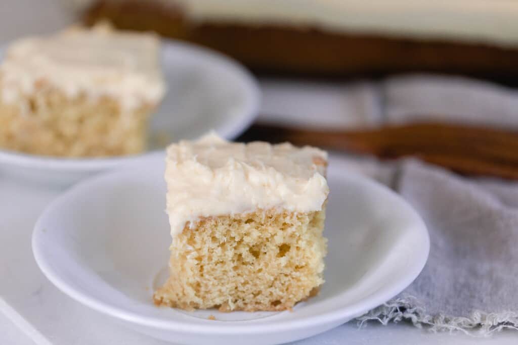 two square slices of sourdough vanilla cake with a thick layer of buttercream frosting on white plates with a gray napkin