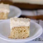 two square slices of sourdough vanilla cake with a thick layer of buttercream frosting on white plates with a gray napkin