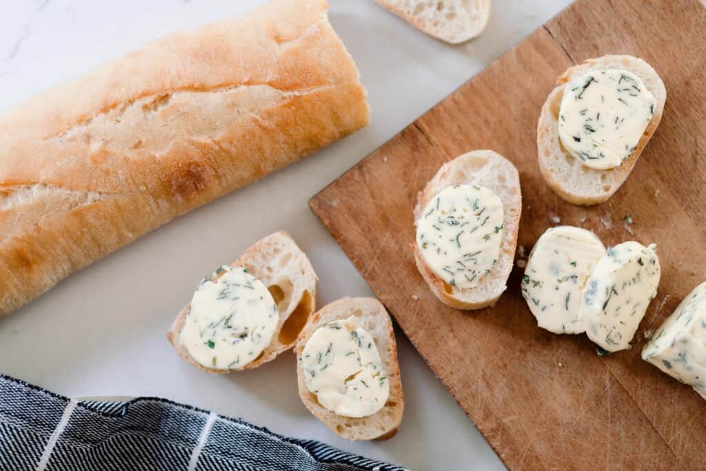 loaf of French bread next to a cutting board with slices of bread with compound butter