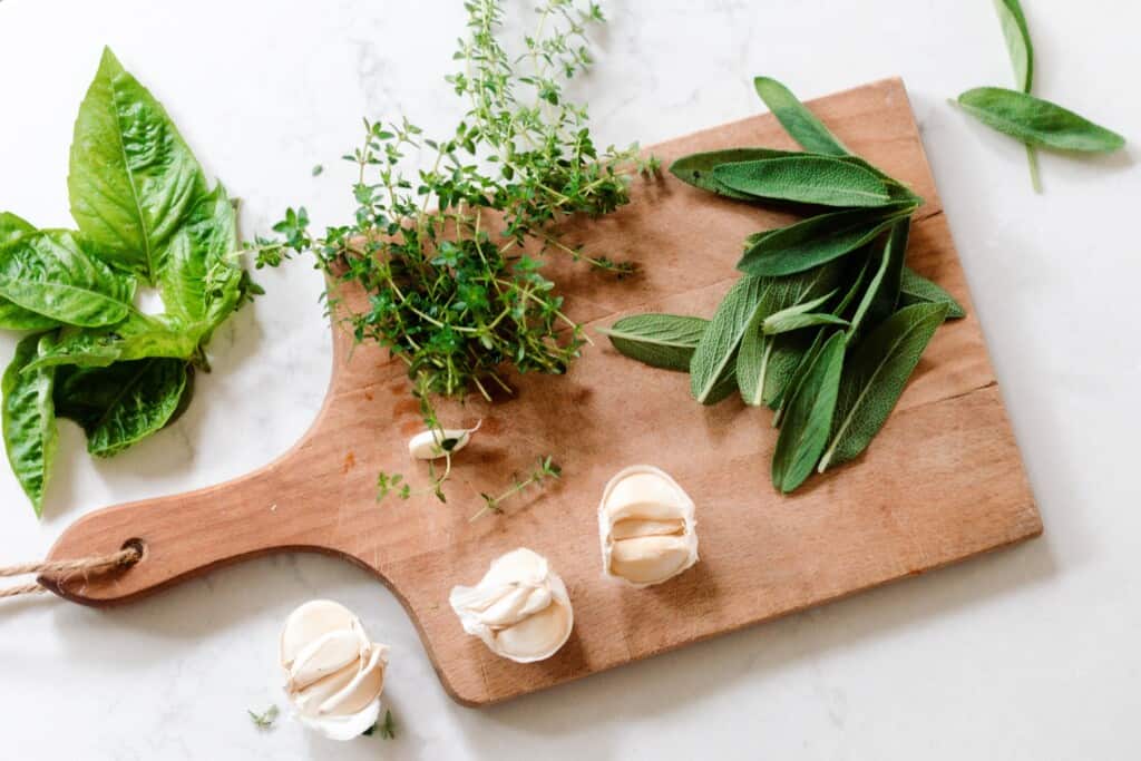 sage, thyme, basil, and garlic on or mourned a wooden cutting board on a white countertop