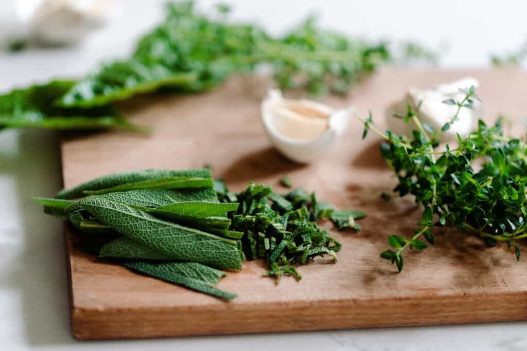 cutting board filled with a variety of fresh herbs and cloves of garlic
