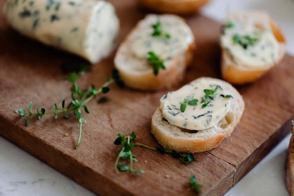 slices French bread topped with compound butter on a wood cutting board with thyme and more herb butter around the bread