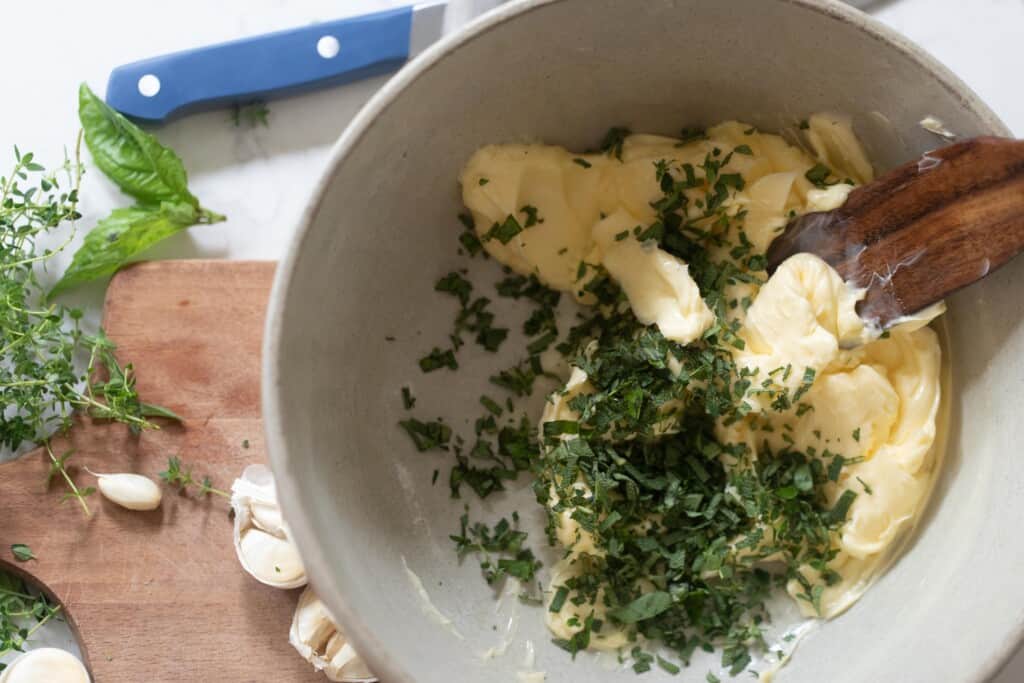softened butter and fresh chopped herbs in a bowl with a wooden spatula.