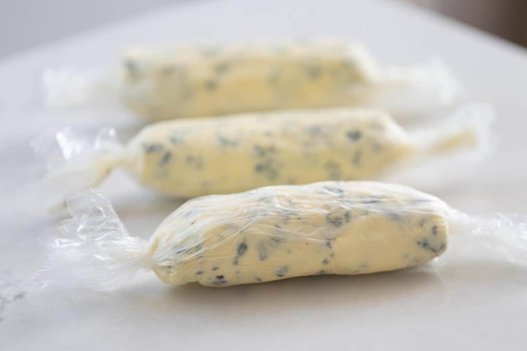 three herb butter logs wrapped in parchment paper on a white countertop