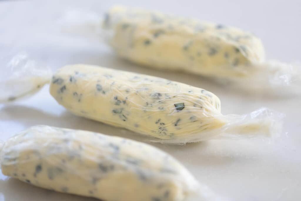 three logs of herb butter wrapped up in parchment paper on a white countertop