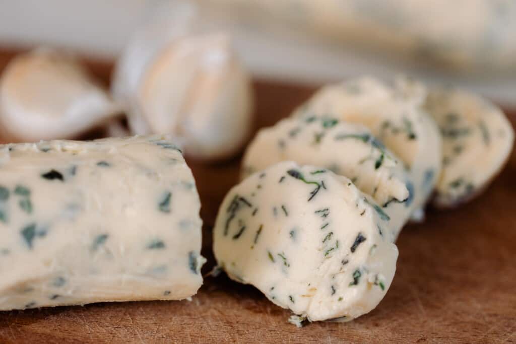 close up picture of slices of herb butter on a wooden cutting board