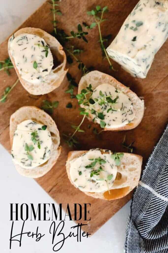 four slices of fresh bread with compound butter on top on a cutting board with herbs spread around and a log of herb butter to the back right