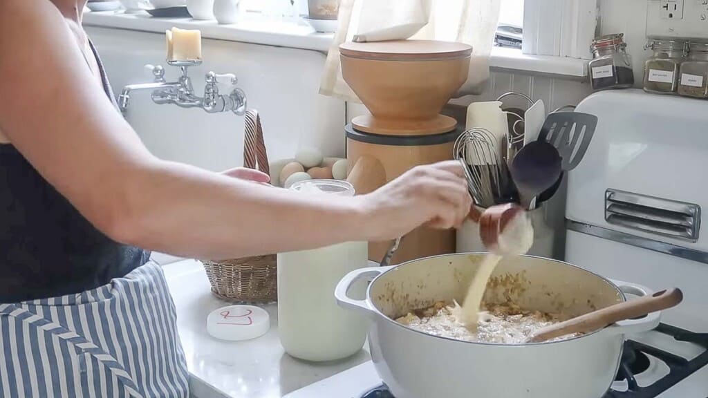 cream being added to peaches and cream oatmeal in a dutch oven on a white vintage stove