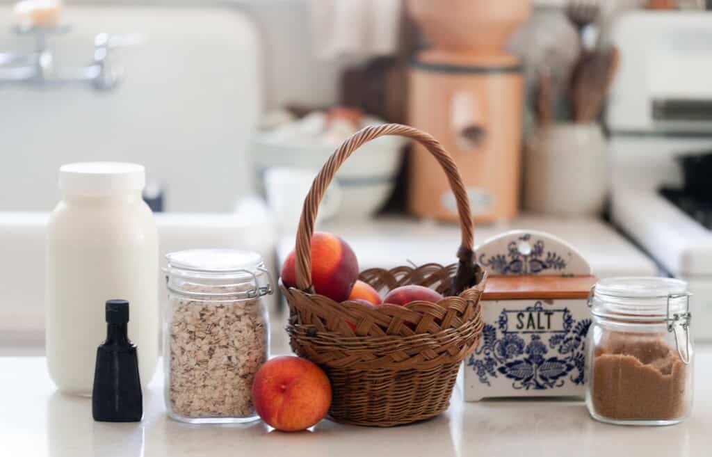 basket full of peaches, jar of oats, jar of brown sugar, and a jar of milk on a white kitchen island