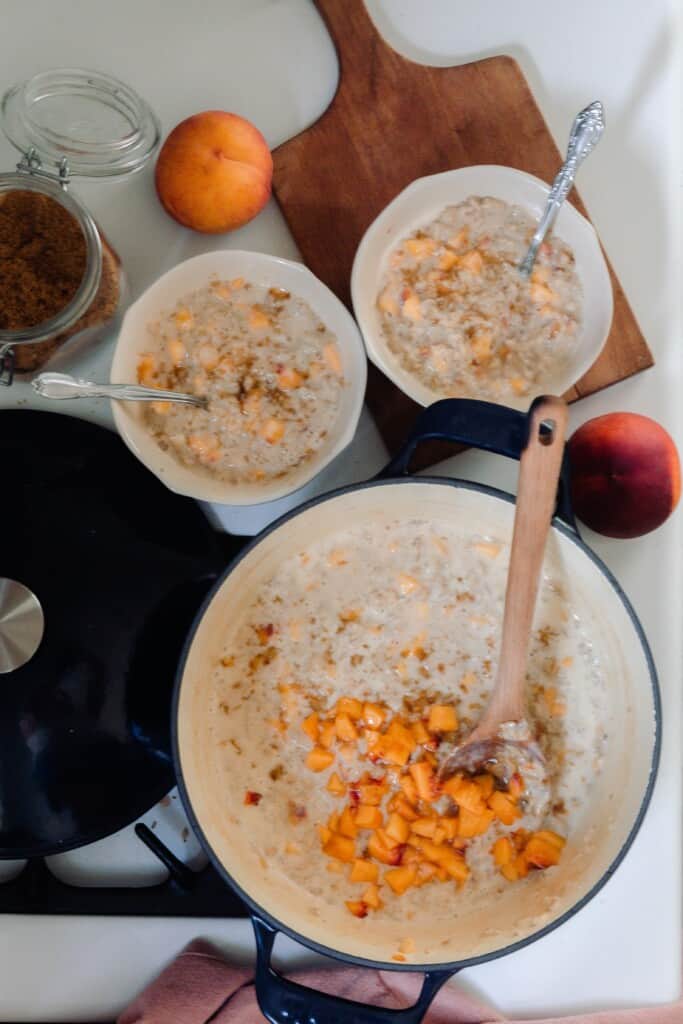a dutch oven and two bowls full of peaches and cream oatmeal on a vintage stove