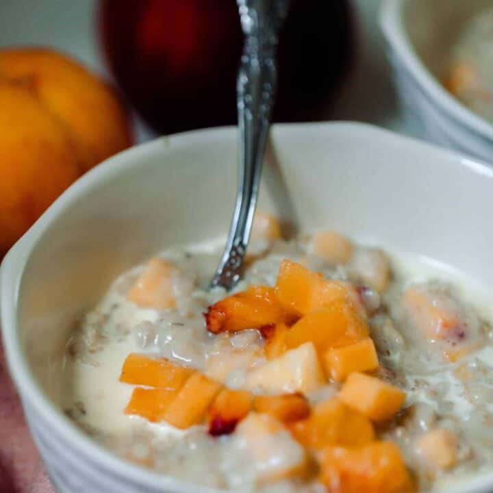 close up of oatmeal with preaches on top I a white bowl with two peaches in the background