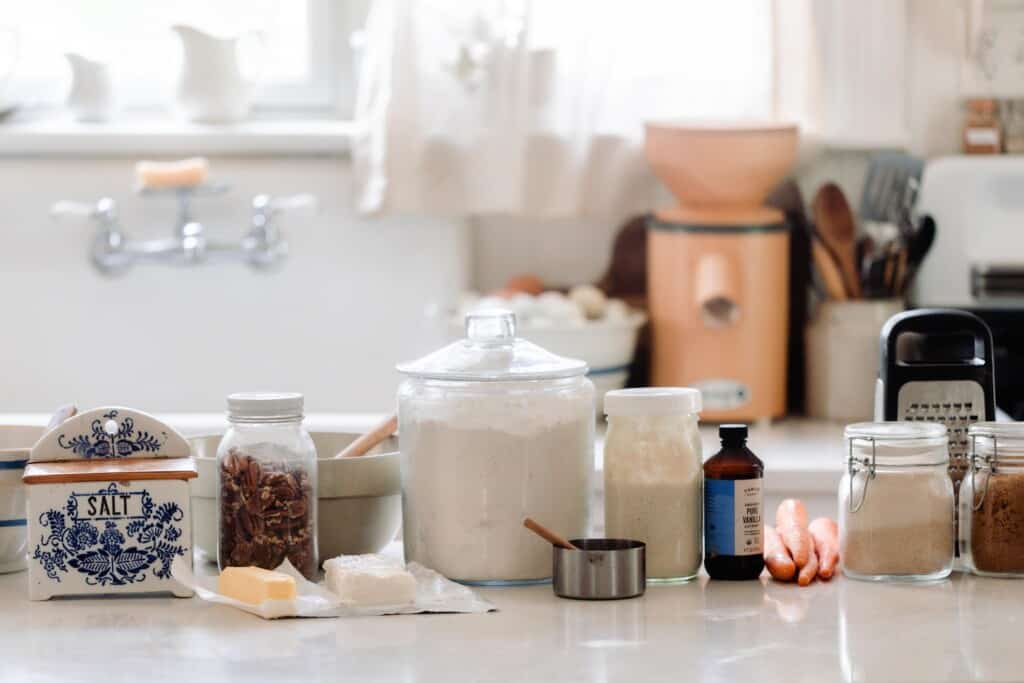 jars of flour, sugar, salt, nuts, vanilla extract, and measuring cups on a white countertop