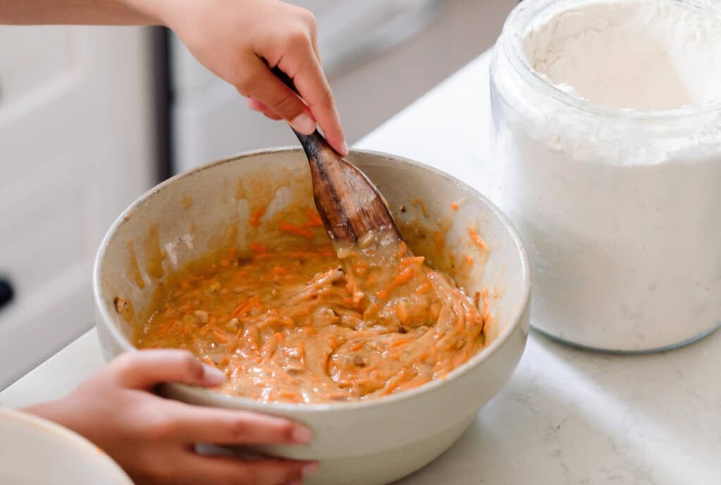 hand stirring sourdough carrot cake batter with a wooden spatula 