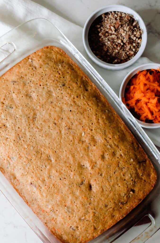 bake sourdough carrot cake in a glass baking dish with two jars of shredded carrots and chopped pecans to the right