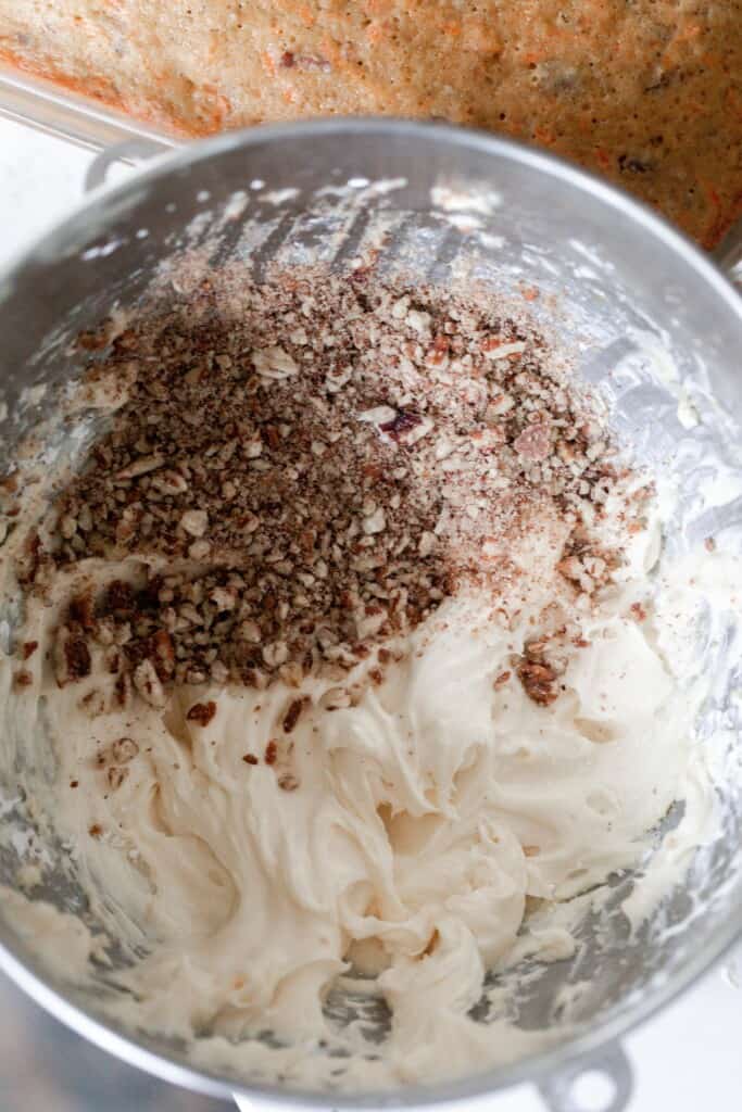 chopped pecans on top of cream cheese frosting in a metal bowl