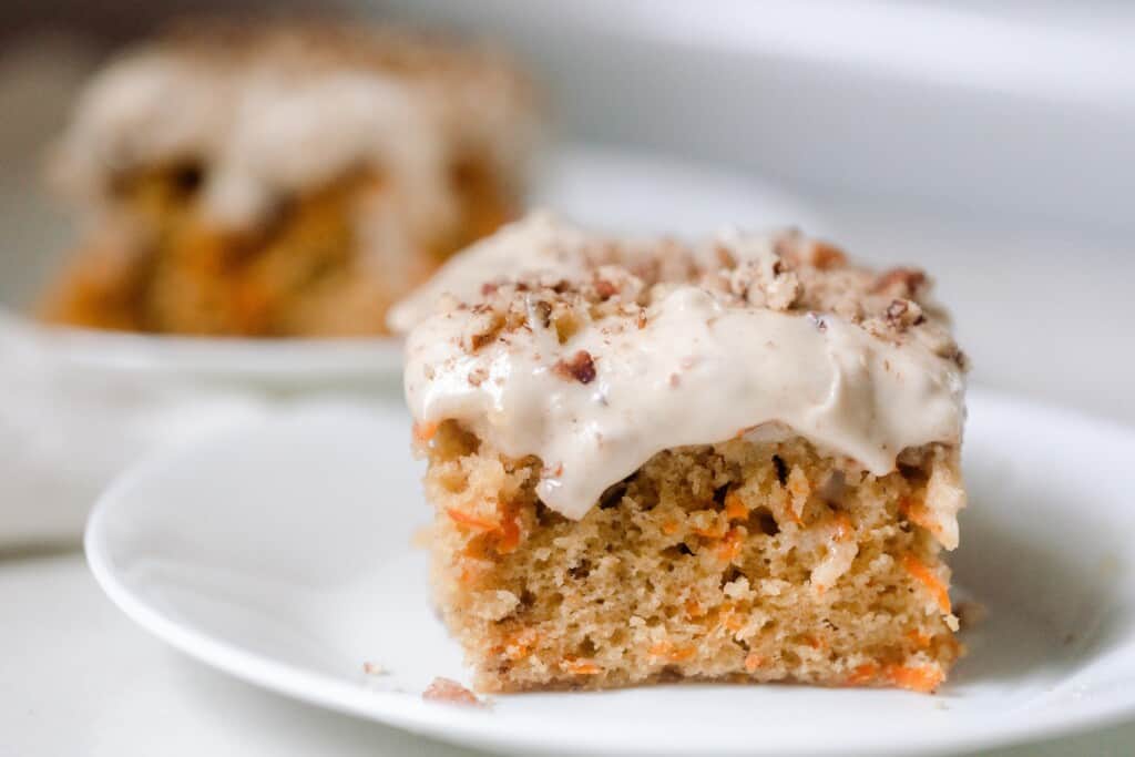 two square slices of sourdough carrot cake topped with cream cheese frosting and pecans on a white plates