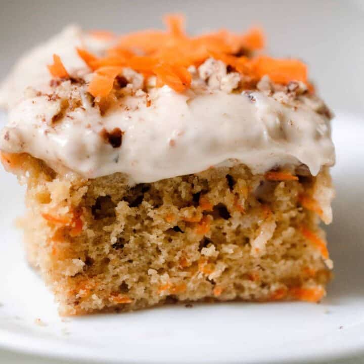 close up picture of a square slice of sourdough carrot cake topped with cream cheese frosting, shredded carrots and pecans