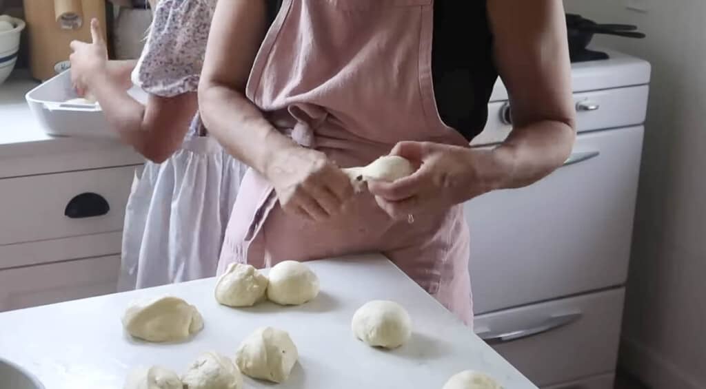 woman wearing a pink apron making rolls on a white countertop