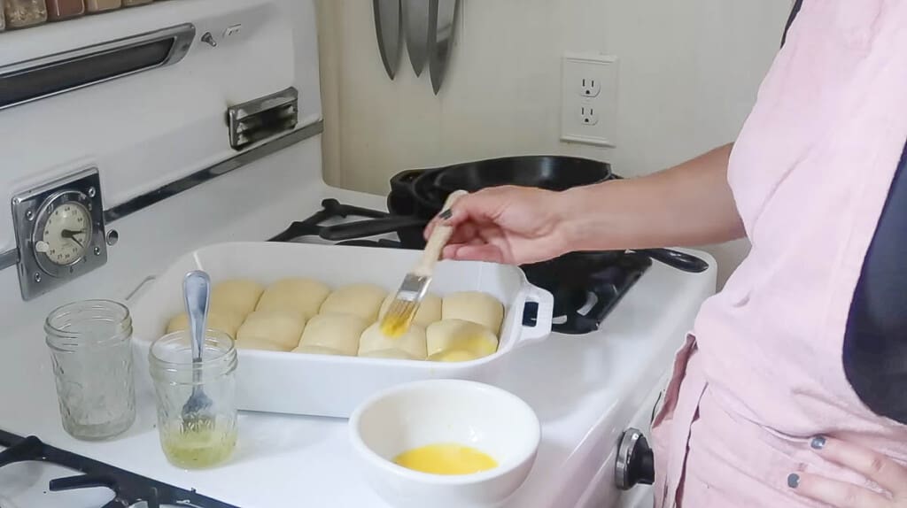 woman brushing the top of rolls in a baking dish with a egg wash