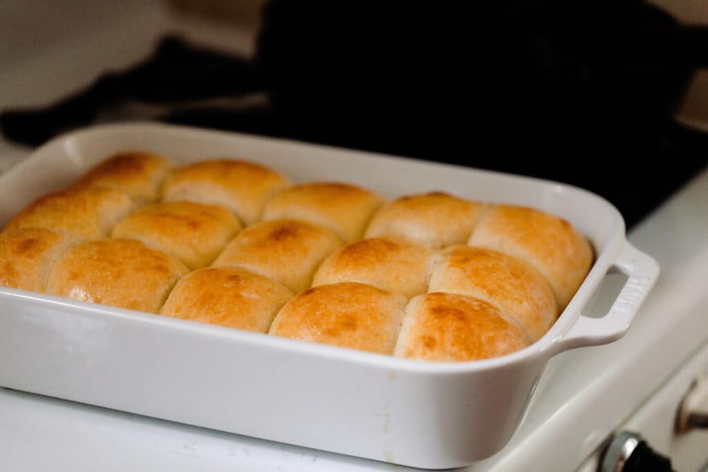 a white ceramic baking dish full of sourdough sweet rolls on a white vintage stove