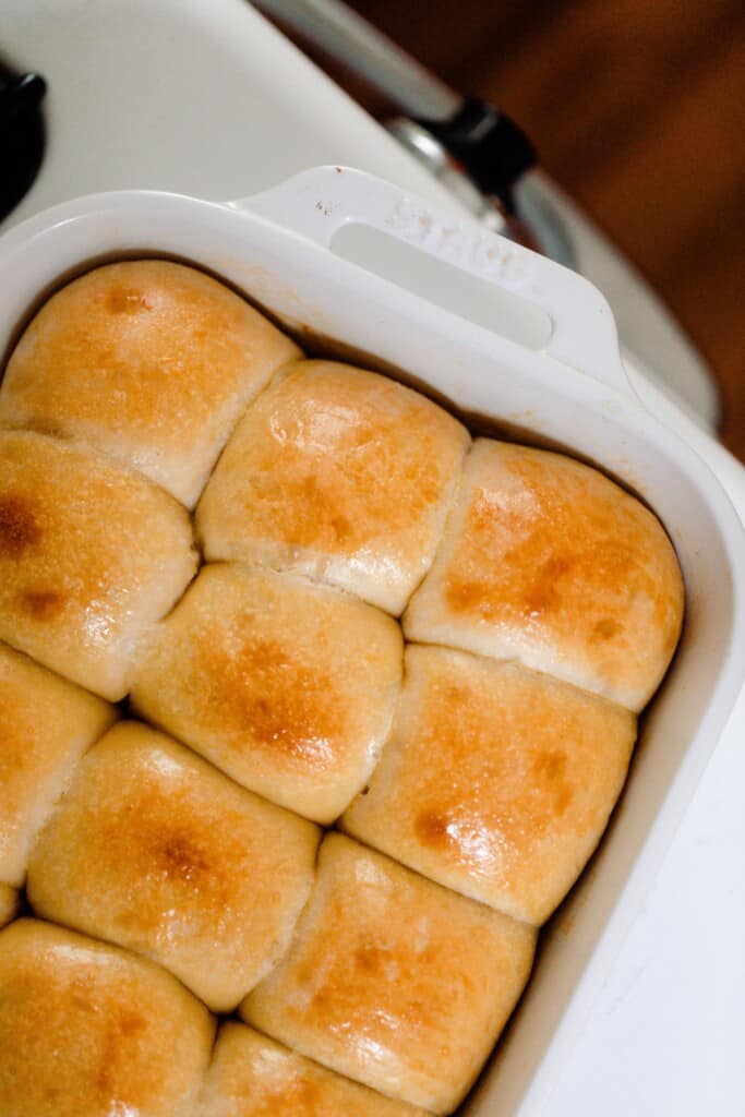 overhead photo of sourdough Hawaiian sweet rolls freshly baked in a white ceramic baking dish on a white vintage stove