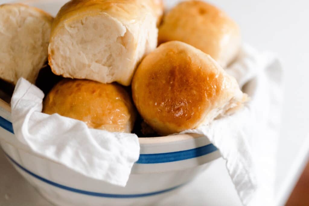 close up picture of sourdough Hawaiian sweet rolls stacked in a blue and white bowl lined with a white linen towel