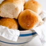 close up picture of sourdough Hawaiian sweet rolls stacked in a blue and white bowl lined with a white linen towel