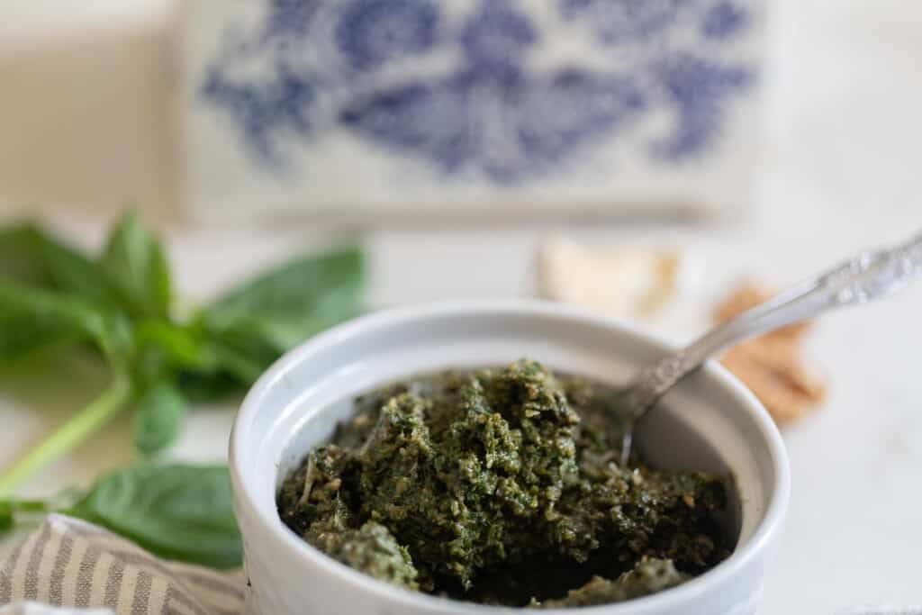 jar of walnut pesto with a spoon. Basil, walnuts, and a salt box in the background