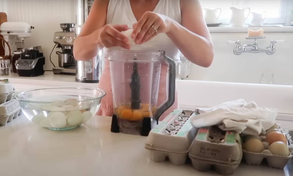 woman cracking eggs into a blender on a white quartz countertop