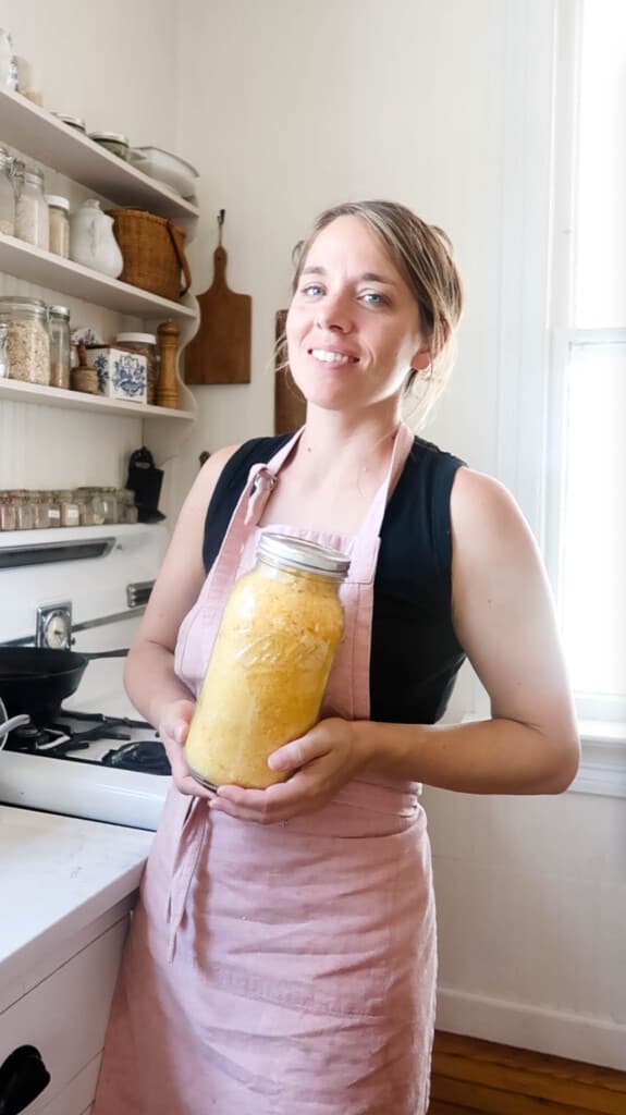 woman in a pink apron holding a half gallon jar of freeze dried eggs in her white farmhouse kitchen