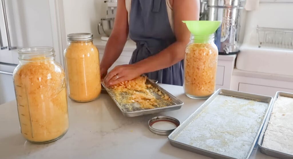 woman taking freeze dried eggs off of a pan and placing them into a half gallon mason jar with funnel