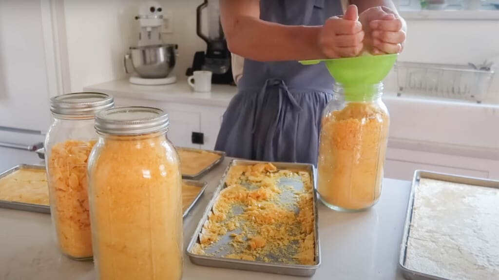 woman adding freeze dried eggs to a mason jar with funnel with more jars of freeze dried eggs around 