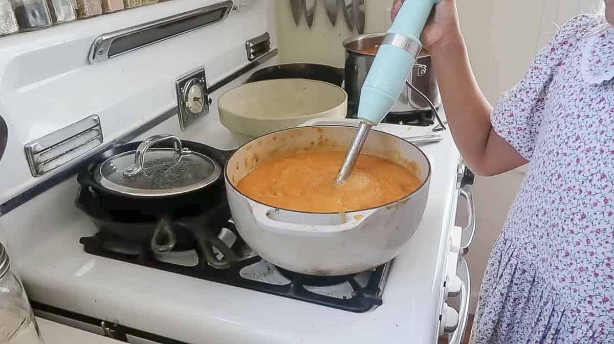Peaches being blended with a immersion blender in a white Dutch oven.