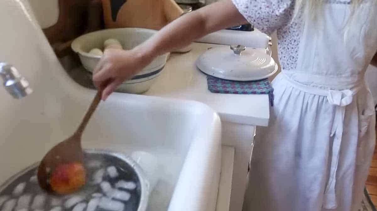 Girl adding a peach to ice water for peeling.