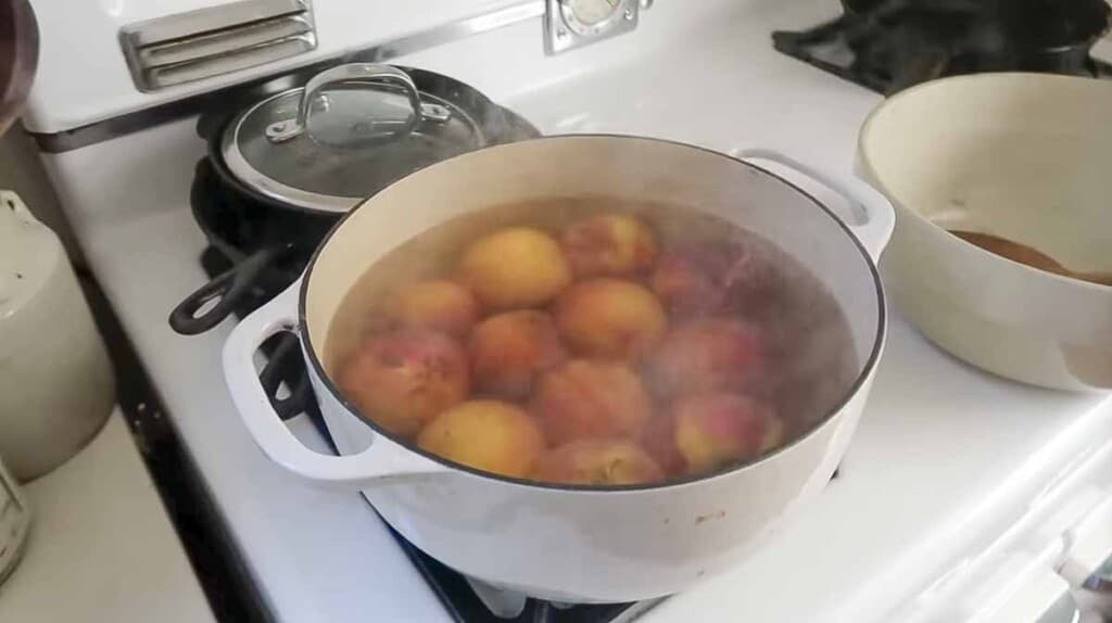 peaches in a white dutch oven filled with water on a white stove