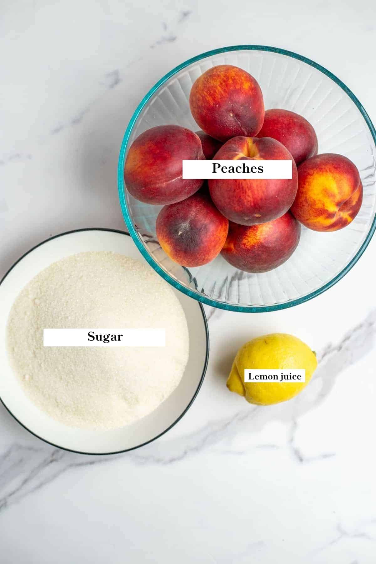 Peaches, sugar, and a lemon on a counter top.