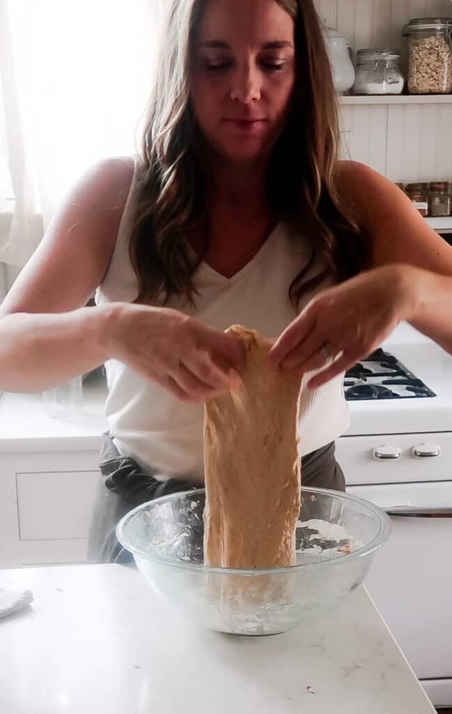 woman performing stretch and folds with sourdough bread dough in a glass bowl