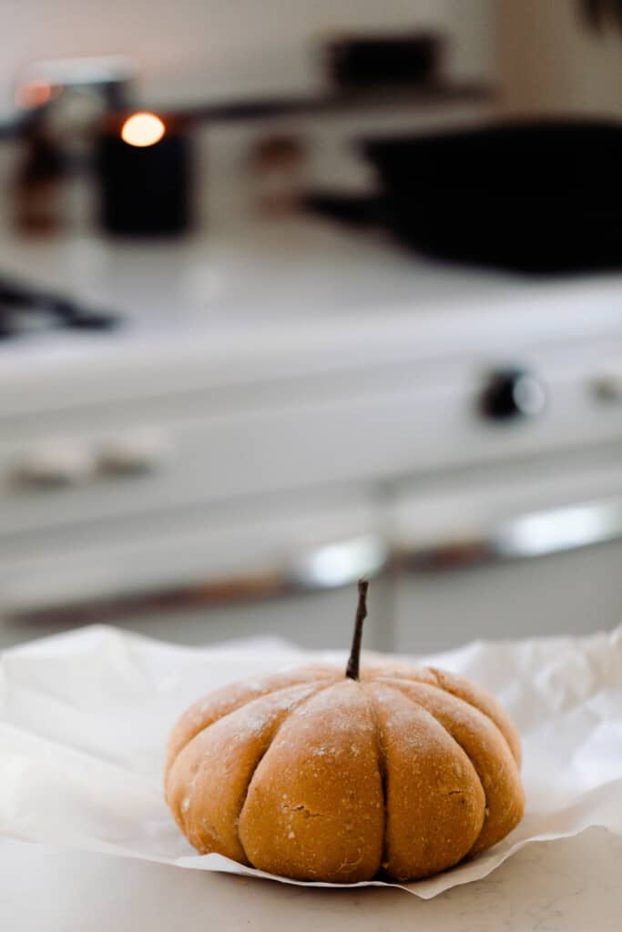 loaf of pumpkin sourdough bread shaped like a pumpkin on parchment paper on a white quartz countertop with a vintage stove in the background
