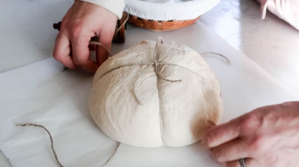 hands tying strings around a sourdough boule on parchment paper