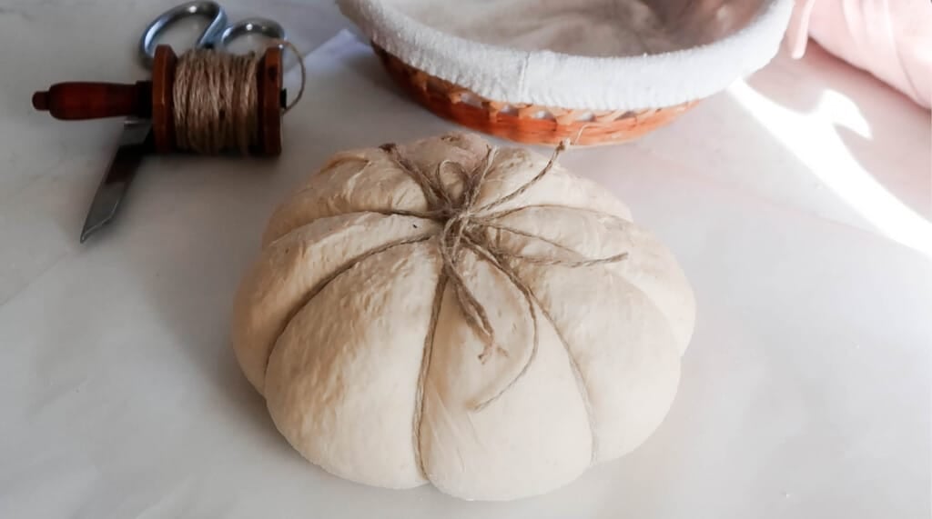 4 pieces of string tied on a sourdough boule on parchment paper